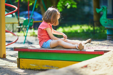 Adorable preschooler girl having fun on playground in sandpit