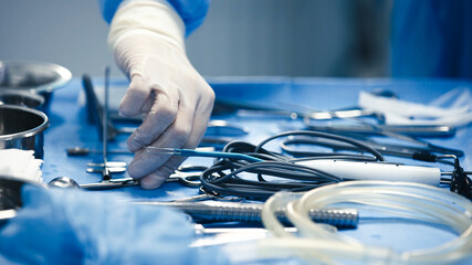 Surgical hand in sterile gloves is carefully selecting instruments from a blue surgical table...