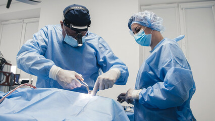 Medical professionals in blue surgical attire are performing a delicate operation in a sterile...