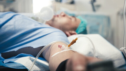Patient receiving medical treatment in a hospital setting, with IV drip and monitoring equipment,...