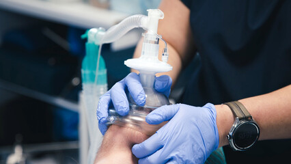 Medical professional in blue gloves is performing resuscitation with a bag valve mask on a patient...