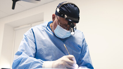 Surgeon in blue scrubs, focused on intricate procedure, wearing surgical mask and magnifying...