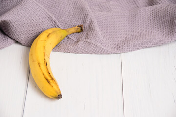One banana with damaged peel and kitchen towel on gray light table. Rescue the lonely banana