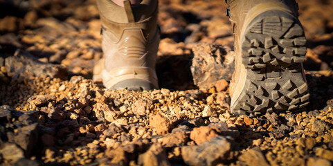 Legs in hiking boots closeup, a girl walks on a rocky desert terrain.