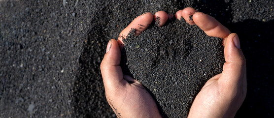 A person is holding a black volcanic sand in his or her hands, closeup view.