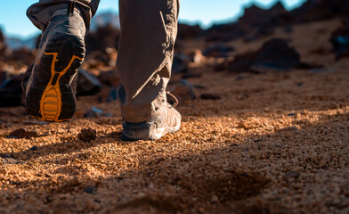 A man walks in a desert among mountains, legs in trekking shoes closeup.
