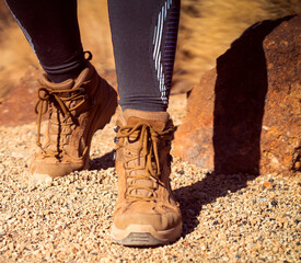 Legs in hiking boots closeup, a girl walks on a rocky desert terrain.