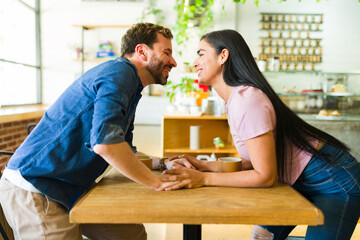 Happy couple holding hands and about to kiss each other in a coffee shop