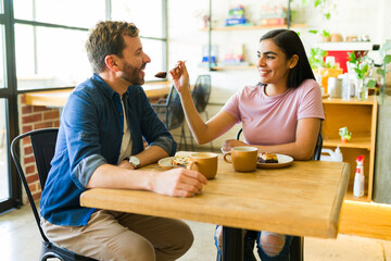 Hispanic couple sharing cake and coffee, enjoying romantic date in cafe