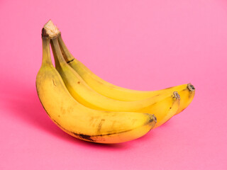 A branch of bananas with spoiled skin on a pink background