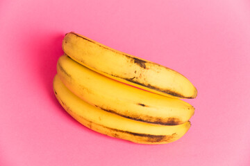 A branch of bananas with spoiled skin on a pink background