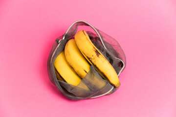 Bananas with damaged peel in an eco-bag on pink background