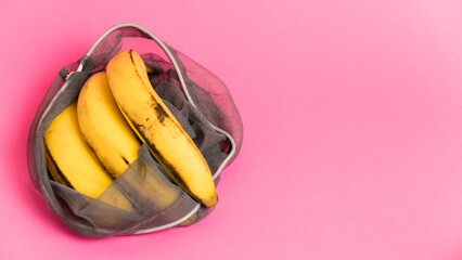 Bananas with damaged peel in an eco-bag on pink background