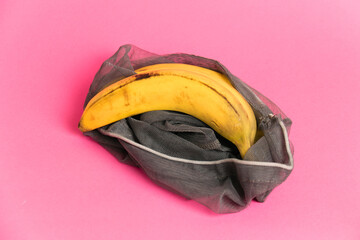 Bananas with damaged peel in an eco-bag on pink background