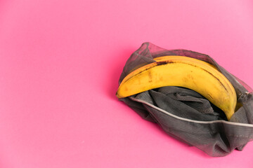 Bananas with damaged peel in an eco-bag on pink background