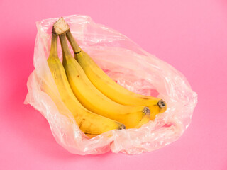 Bananas with spoiled skin in a plastic bag on a pink background