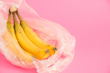 Bananas with spoiled skin in a plastic bag on a pink background