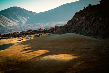 A desert landscape with sandy valleys among mountains and volcanoes at sunset.