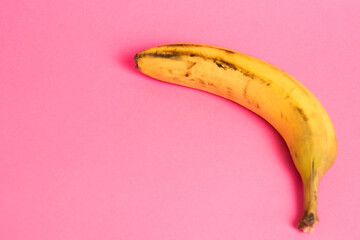 Banana with spoiled skin on pink background. Save the lonely banana