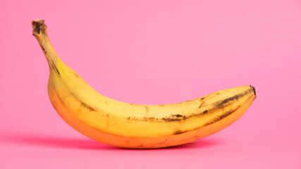 Banana with spoiled skin on pink background. Save the lonely banana