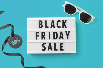 Black friday sale concept, word lightbox with black price tag and black ribbon and sunglasses on blue background