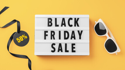 Black friday sale word lightbox with discount tag and black ribbon and sunglasses on yellow background