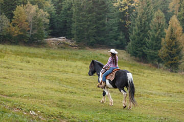 Authentic western scene of a confident cowgirl on horseback, riding through scenic mountain terrain under a light mist