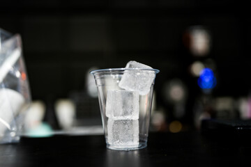 Fill of three square ice cubes in empty plastic glass for mixing cocktail at restaurant.