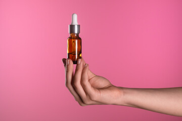 Hand Holding Dropper Bottle Against Vibrant Pink Background