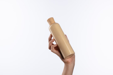 Hand Holding Beige Shampoo Bottle Against White Background