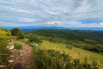 A scenic view from the hills towards Shiljak, mountain Rtanj in Serbia, showcasing lush greenery and rugged terrain under a dynamic sky.