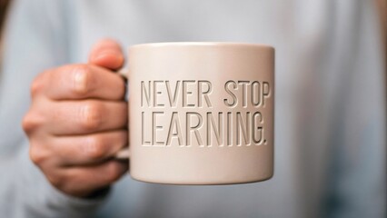 A close-up image of a hand holding a beige mug with the motivational phrase "Never Stop Learning" printed on it.