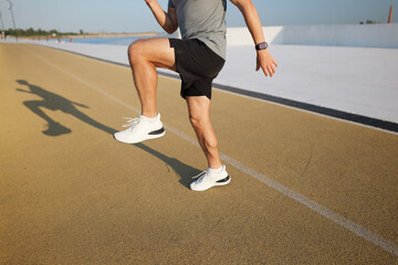 Runner engaging in warm-up exercises on a track at sunrise