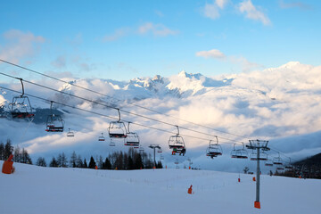 Passo Tonale, Italy - 28.01.2023: Red cable cars moving over snow-covered mountain landscape, leading to distant station building, with the snowy terrain and tracks visible below, alpine ski resort
