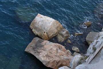 Massive rocks sit at the edge of the deep blue sea, with waves gently lapping against their rugged...