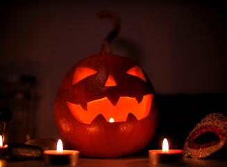 A carved Halloween pumpkin. Jack-o'-lantern glowing with a candle inside on a surface with...