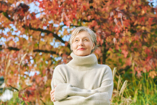 Outdoor portrait of happy mature 55 - 60 year old woman in autumn park, wearing beige pullover.  Active and healthy lifestyle