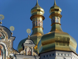 Golden domes of an Orthodox church in Kyiv with religious frescoes and intricate details against a clear blue sky