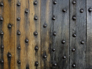 Close-up of an aged wooden door with iron studs in vertical alignment showing natural wear