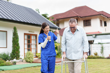 Home caregiver supports elderly man using walker outdoors with encouragement and positive...