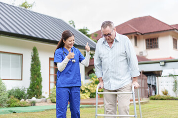 Home caregiver supports elderly man with walker outdoors, showing encouragement and positive...