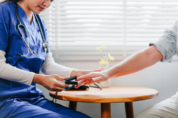 Home caregiver in blue uniform checking elderly patient blood pressure in bright room, showing care...