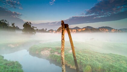 Ethereal Dawn Over a Misty River with Sunlit Peaks and Ruined Posts