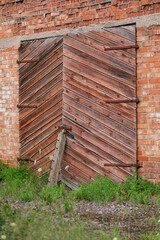 The photo shows a close-up of old wooden gates with diagonal planking set into a brick wall.
