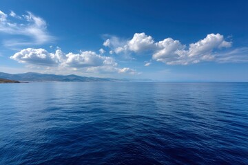Fototapeta premium Still deep blue sea under a partly cloudy sky with distant land visible on the horizon