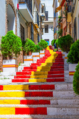 Spanish Steps Spanish flag stairs staircase narrow pedestrian Calle Puchalt street with colorful typical buildings houses in old town Calpe city historical centre in sunny summer day, Spain