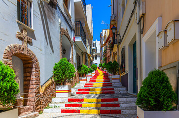 Spanish Steps Spanish flag stairs staircase narrow pedestrian Calle Puchalt street, colorful typical buildings houses in old town Calpe city historical centre in sunny day, Valencian Community, Spain