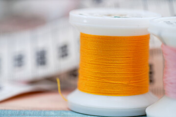 Bright orange thread spool and measuring tape used in crafting projects at a sewing workspace during daylight hours