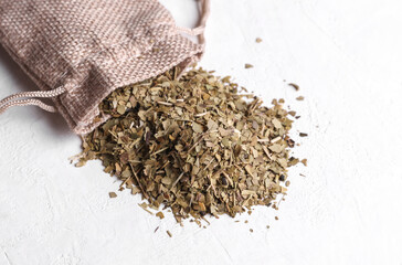 Dry yerba mate in a miniature burlap bag on a white concrete background