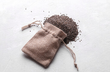 Chia seeds in miniature burlap bag on white concrete background